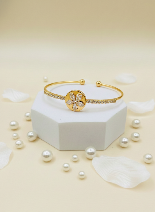 Gold bracelet with decorative element on a white hexagonal base surrounded by pearls on a beige background