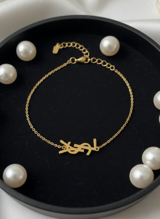 Gold bracelet with a unique design on a black dish surrounded by pearls.