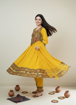 Woman in a yellow traditional outfit with intricate patterns, standing against a plain background.