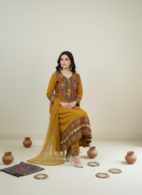 Woman wearing a mustard yellow traditional outfit with intricate patterns, sitting on a white floor with decorative pots and rugs.