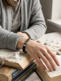 Person wearing a bracelet on a marble surface with books and glasses.
