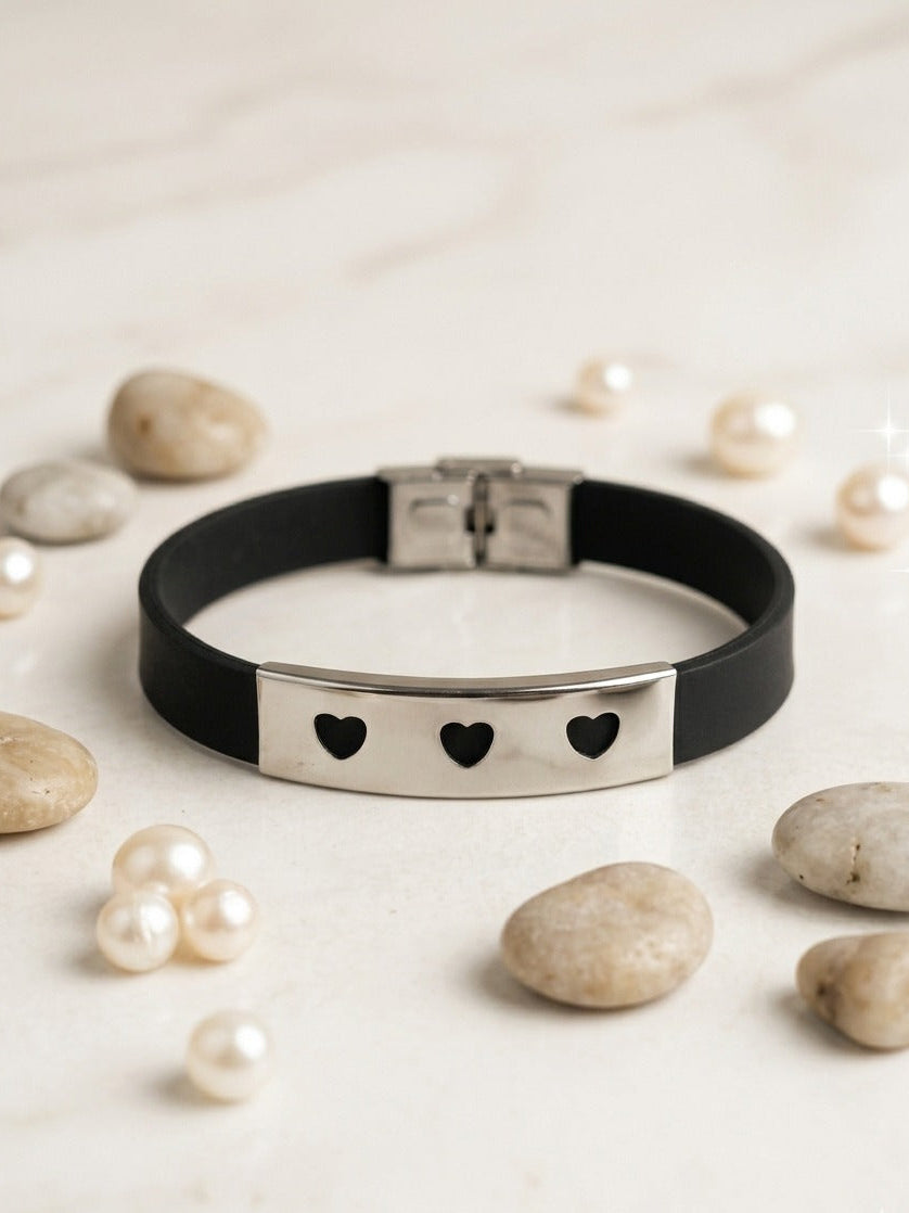 Black bracelet with heart-shaped cutouts on a light background with pearls and stones.