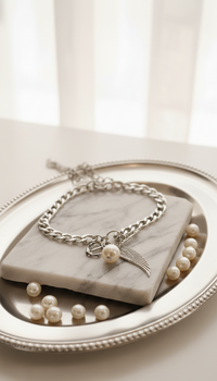 Silver bracelet with a bow charm on a marble surface with pearls.