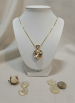 Gold necklace with a heart-shaped pendant on a white mannequin bust, surrounded by buttons on a light background.