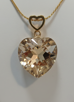 Heart-shaped crystal pendant on a gold chain against a light gray background