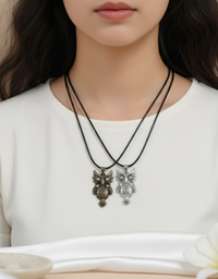 Two owl-shaped necklaces on a person wearing a white top.