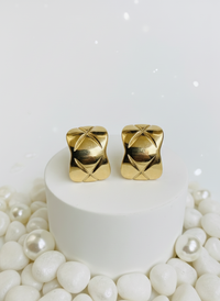 Gold earrings on a white pedestal with pearls around