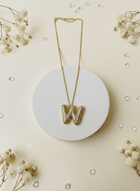 Gold necklace with 'W' pendant on a white round base surrounded by small flowers and crystals.