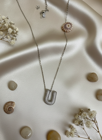 Silver necklace with a pendant on a beige fabric background with seashells and flowers.