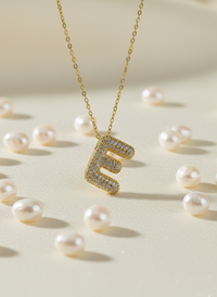 Gold necklace with a letter 'E' pendant surrounded by pearls on a light background