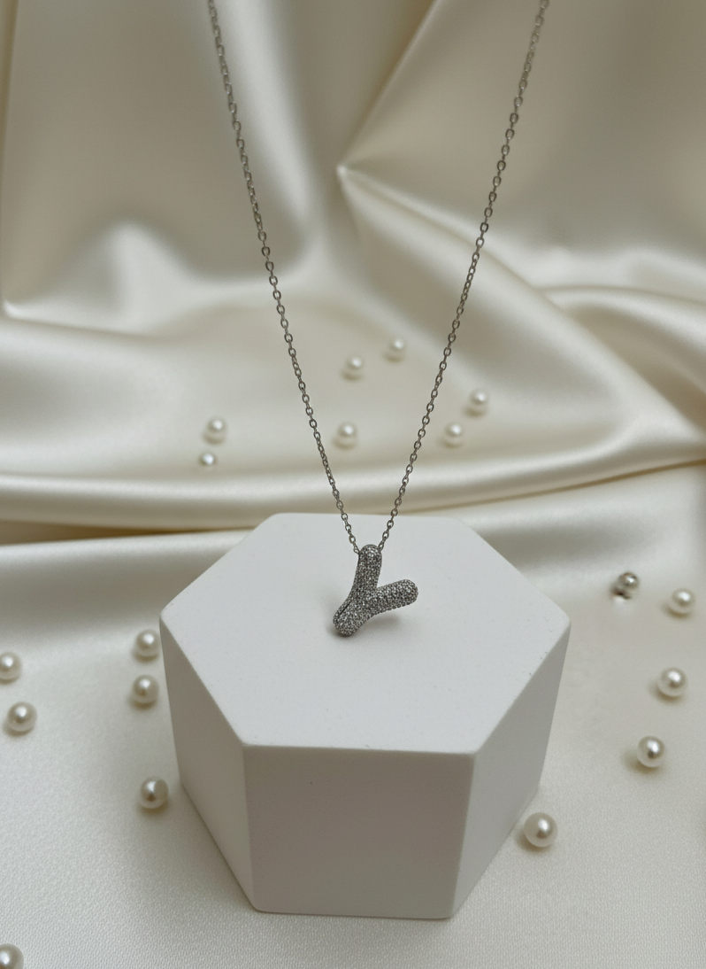 Necklace with a pendant on a white hexagonal stand against a beige fabric background with scattered pearls.