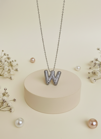 Necklace with 'W' pendant on a beige stand surrounded by small pearls and flowers