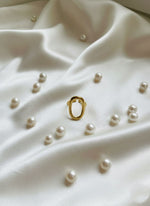 Gold ring surrounded by pearls on a white fabric background