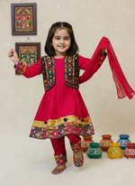 Young girl in traditional outfit with colorful jacket and red dress, standing against a light background with decorative pots.