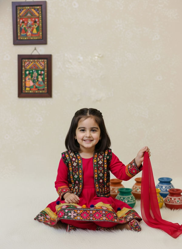 Young girl in traditional outfit holding a red scarf with decorative wall art in the background