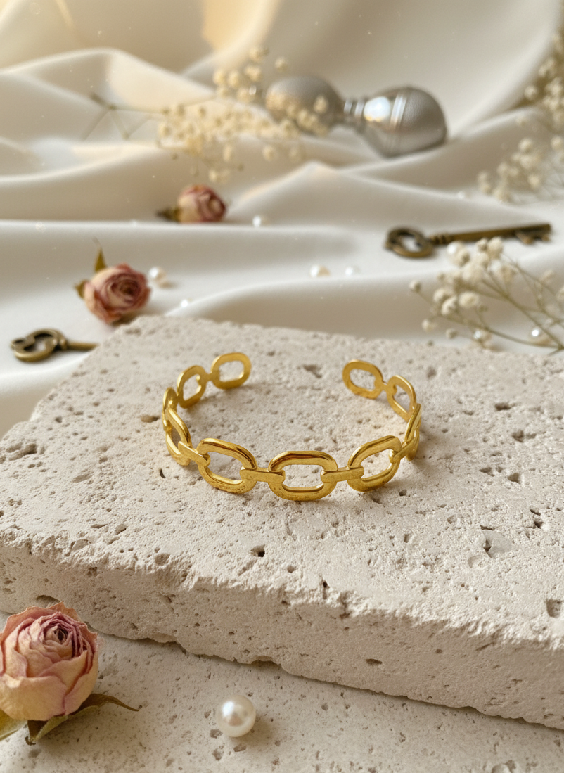 Gold chain bracelet on a textured stone surface with flowers and keys in the background