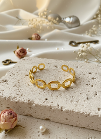 Gold chain bracelet on a textured stone surface with flowers and keys in the background
