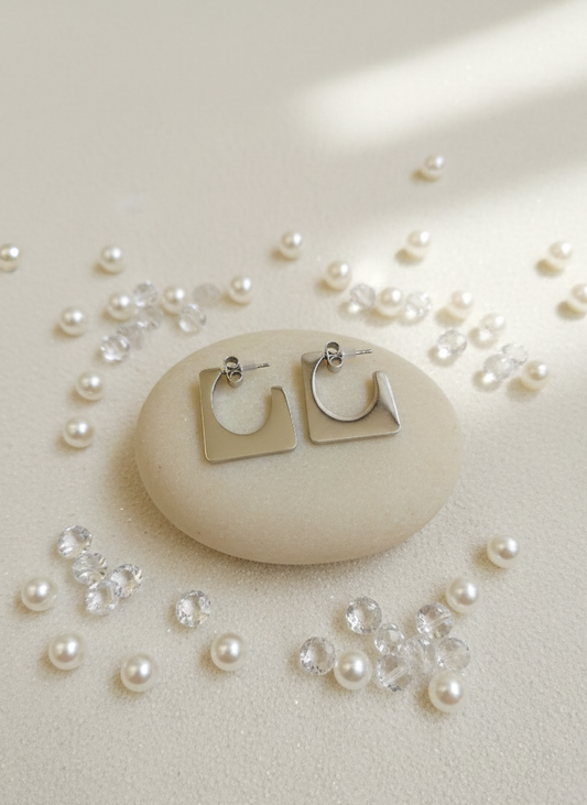 Silver hoop earrings on a stone with scattered pearls and crystals