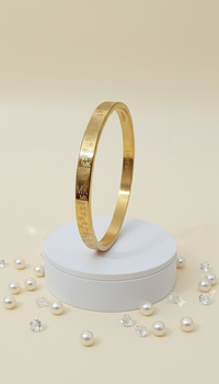 Gold bracelet on a white stand with scattered pearls on a beige background