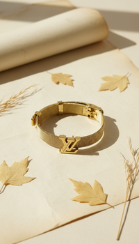 Gold bracelet with a brand logo on a beige surface with leaves