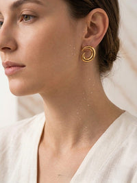 Close-up of a person wearing gold hoop earrings with a neutral background