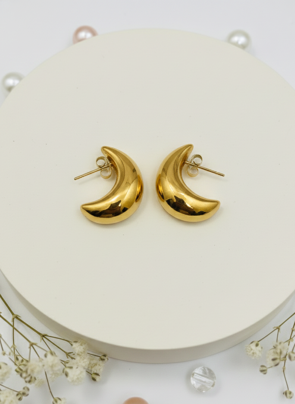 Gold moon-shaped earrings on a white surface with small flowers.