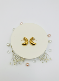 Gold moon-shaped earrings on a white stand with small pearls and crystals.