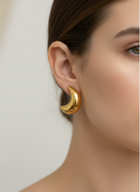 Gold hoop earring worn by a model on a plain background