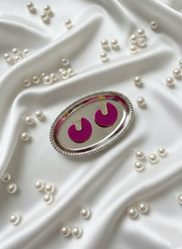 Pink earrings in a silver holder on a white fabric background with pearls.