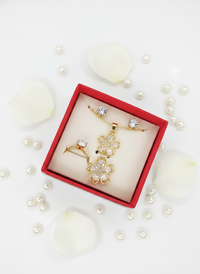 Gold floral earrings in a red box with pearls and seashells on a white background