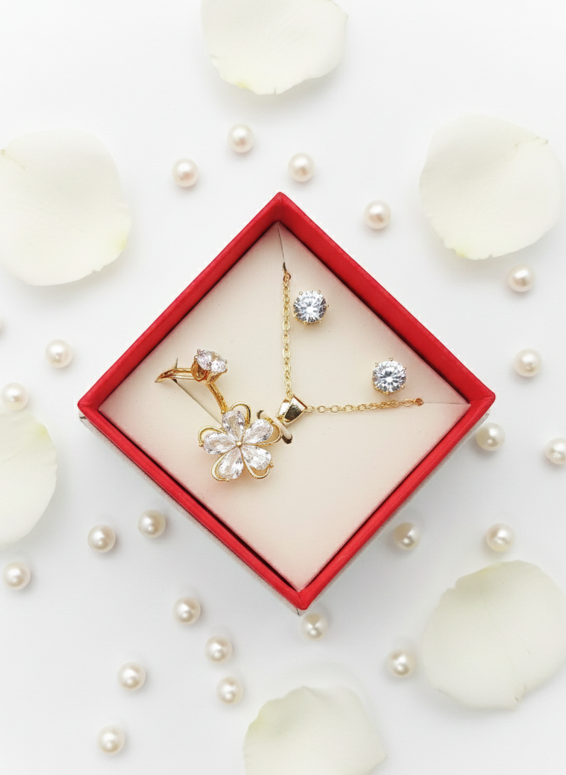 Gold jewelry set with floral design in a red box on a white background with pearls.