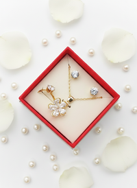 Gold jewelry set with floral design in a red box on a white background with pearls.