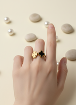Hand wearing a gold ring with a black star design on a beige background with pearls and stones.