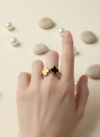 Hand wearing a gold ring with a black star design on a beige background with pearls and stones.