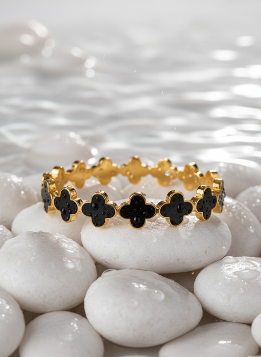 Gold ring with black clover-shaped stones on white pebbles