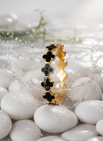 Gold and black floral-patterned rings on white stones with water splash