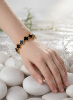 Hand wearing a black and gold bracelet on white pebbles with water splashes