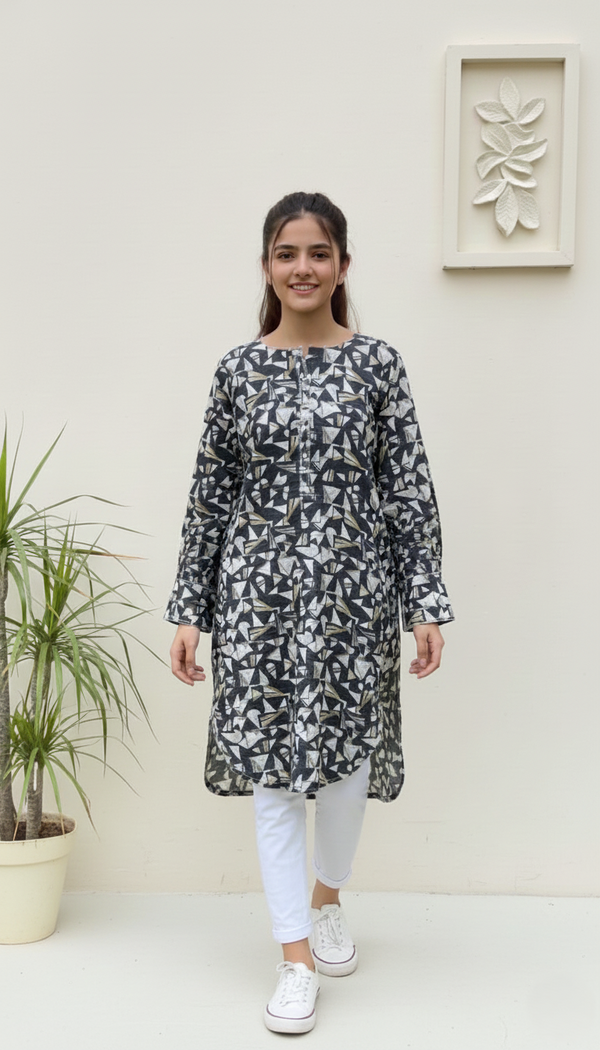 Woman wearing a patterned kurta with white pants standing against a light-colored wall.