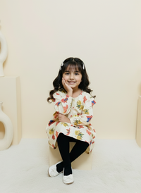 Young girl sitting on a white surface wearing a floral dress.