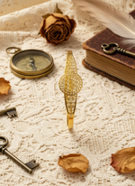 Gold decorative object on a textured surface with keys, rose petals, and a book.