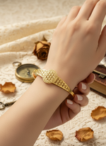 Gold bracelet on a hand with dried roses and a compass in the background
