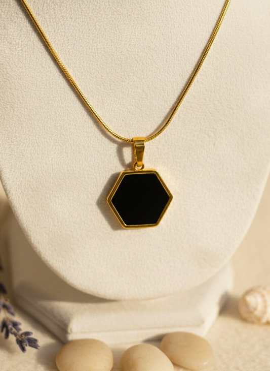 Gold necklace with a black hexagonal pendant on a white stand.