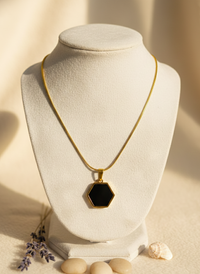 Gold necklace with a black hexagonal pendant on a white mannequin bust against a beige background.