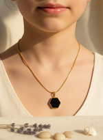 Gold necklace with a black hexagonal pendant on a neutral background