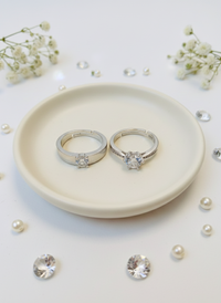 Two silver rings on a white plate with small flowers and pearls around.