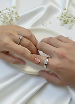 Two hands wearing silver rings on a white fabric background