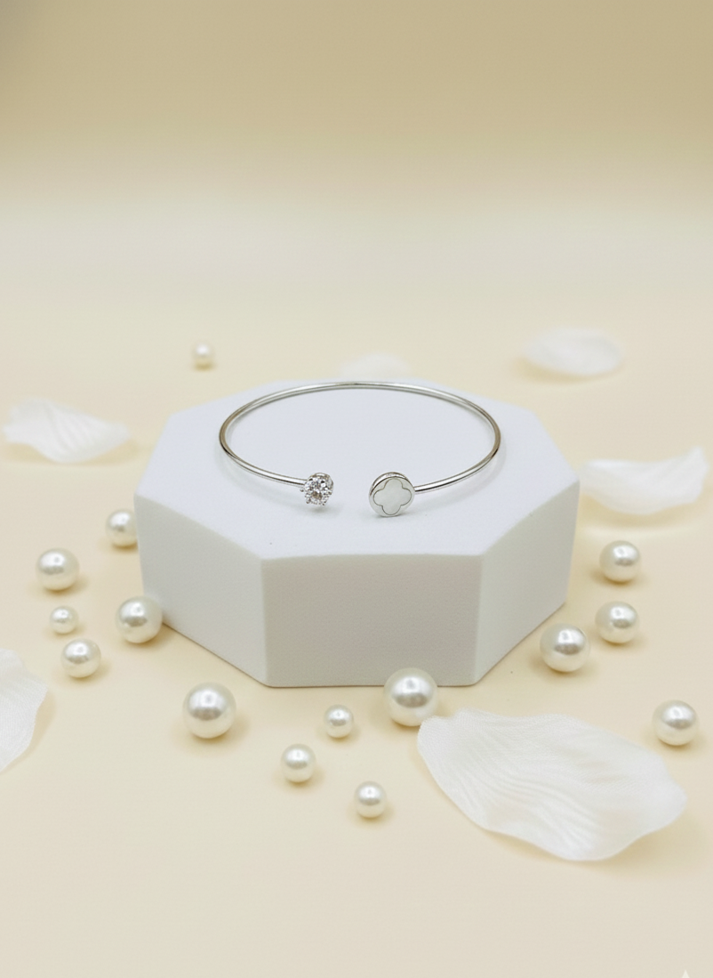 Silver bracelet on a white hexagonal stand with scattered pearls on a light beige background