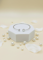 Silver bracelet on a white hexagonal stand with scattered pearls on a light beige background