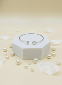 Silver bracelet on a white hexagonal stand with scattered pearls on a light beige background