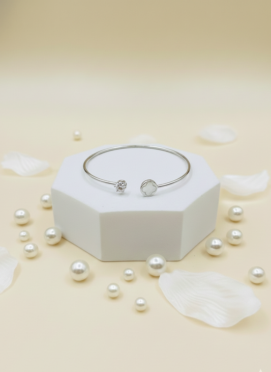 Silver bracelet on a white hexagonal stand with scattered pearls on a light beige background